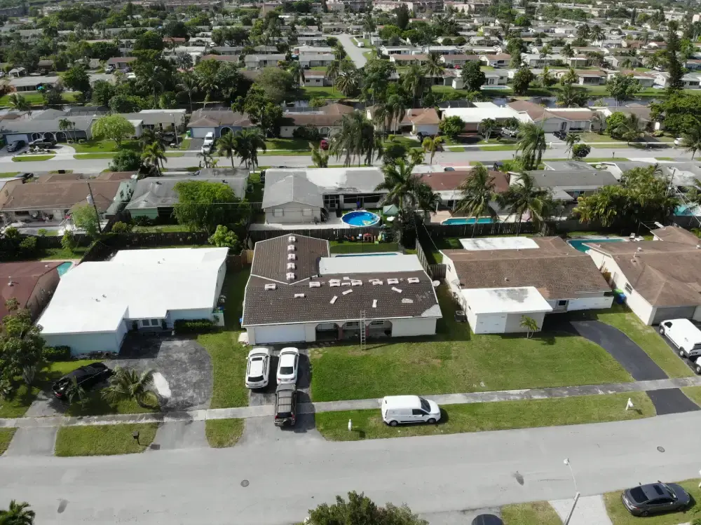 Aerial view of a South Florida neighborhood with roofing material staged on a single-story home mid-replacement