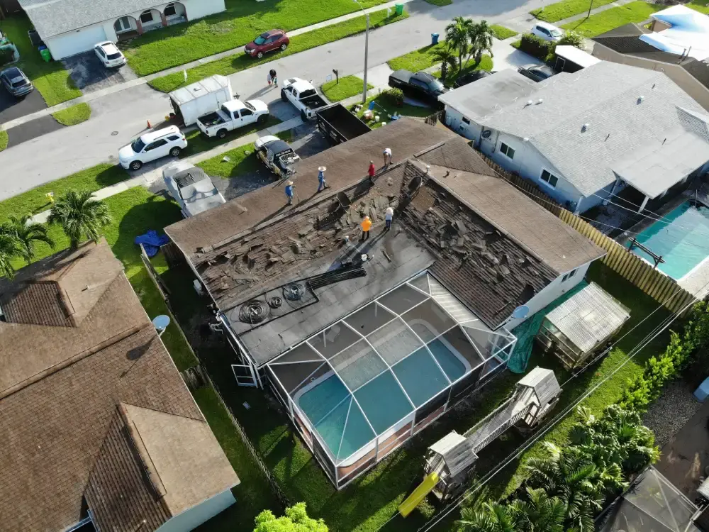 Aerial view of a tear-off in progress with the crew on the roof deck and work trucks at the curb