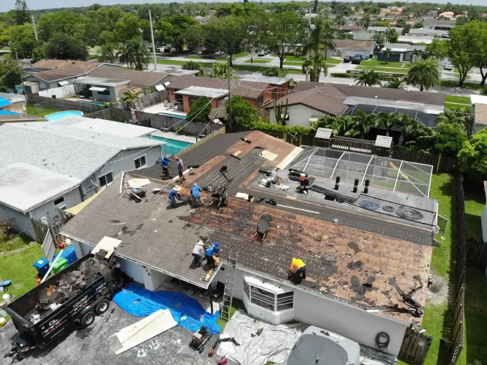Aerial view of a South Florida street with one roof stripped to the bare deck mid-replacement