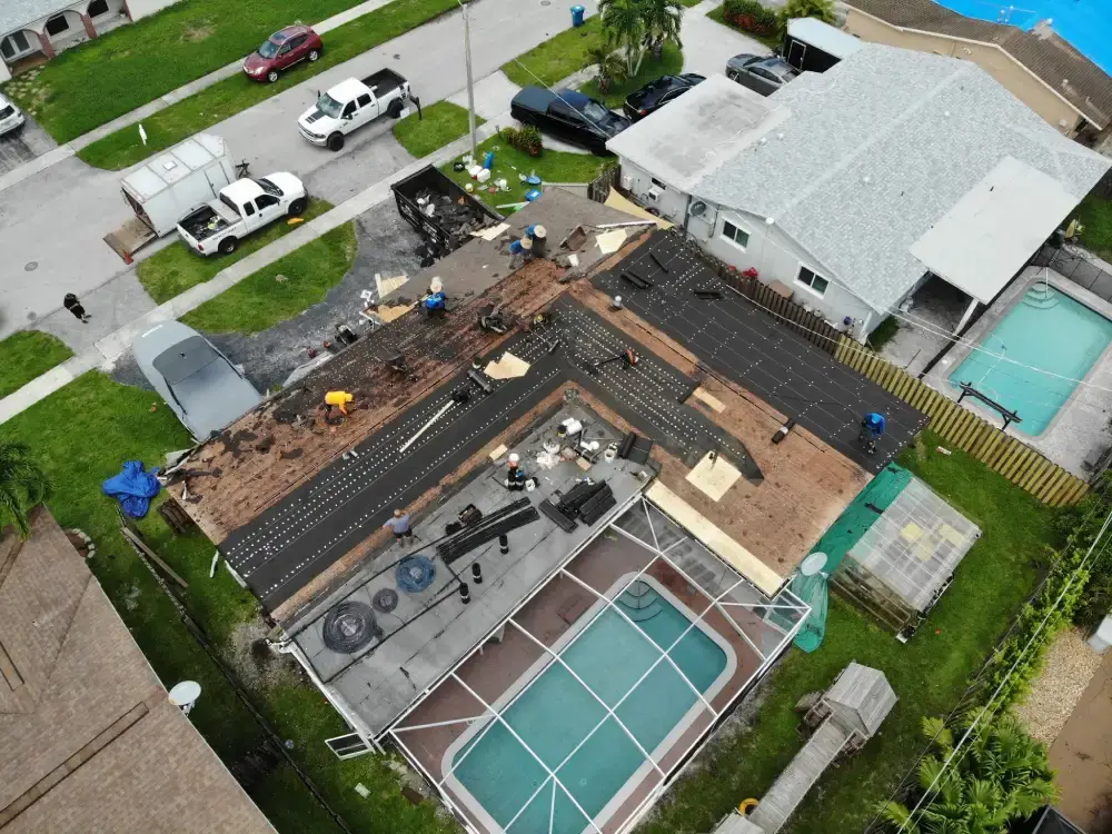 Aerial view of a South Florida home stripped to the roof deck with work trucks lined up at the curb